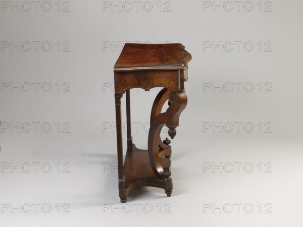 Console, Biedermeier and Louis Philippe styles, mahogany-veneered console on four angular legs mounted on a platform with a wavy outline; front legs strongly curved, rear legs straight and flattened, with bases and capitals; entire piece polished. Platform supported by four low turned legs. Lower sections of legs are channelled and decorated at top and bottom with knobby pinnacles. Wide frame repeats the concave–convex shape of the top, rounded at front corners, wavy-cut at bottom, framed with a half-cylinder; front frame forms the face of the drawer. Top has a profiled edge connected to the frame with cube side panels. Drawer contains two rows of compartments inside; small front-corner compartments have rosewood covers. Drawer secured with a single-bolt mortise lock. Dated 1835–1850. Furniture table. Dimensions: height 82 cm, width 107.2 cm, depth 45 cm., A wooden side table with a polished brown surface and carved curved supports, showing wood grain variations in darker and lighter b...