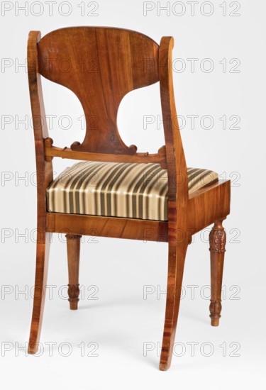 Chair, acanthus ornament, Biedermeier style, palmettes ornament. Mahogany chair with a padded seat removable cushion and a board backrest. Straight front legs, turned in the form of a baluster; sabre-shaped rear legs. Trapezoidal seat, slightly bulging at the front. Wide side frames embrace the seat cushion. The cushion rests on a pine frame, upholstered in green-striped fabric. The backrest consists of angular, S-shaped side stiles, a lower crossbar, and a rounded central board placed between them, narrowed at the bottom, straight in line with the back. The backrest stiles are widened in the lower section, ending at the top with a forward-curved volute. Polished frame enriched with carving — acanthus leaves on the upper part of the front legs, antemion and symmetrical S-shaped beams at the bottom of the backrest boards, scrollwork at the ends of the backrest crossbars. Dated 1830–1840, Warsaw?; Poland. Seating furniture; furniture. Dimensions: height 92 cm, width 51.6 cm, depth 56.5 c...