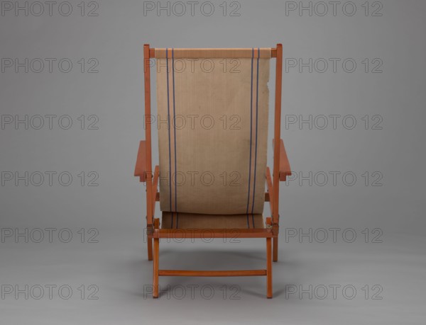 Deckchair, Polish Timber Industry, Czerski and Jakimowicz furniture factory; 1929–1939,  furniture factory author; lounge, beach, and garden folding deckchair constructed from two different-sized rectangular frames: the backrest smaller and the seat larger, connected by hinges, with canvas stretched over them. Frame elements except the turned rear leg connector and the doubled front seat stile are angular. The seat frame is supported on its shorter sides by two folding legs connected by a connector, the front extended into armrest supports. Armrests have hinges adjustable in three positions. Salmon-colored canvas fabric with vertical orange stripes framed by narrow blue stripes; canvas attached to the underside of the upper backrest frame and the rear seat frame, sandwiched between the two front seat frames. Originally equipped with a separate footrest. 1938–1939; Lviv place of origin; seating furniture; height 84.2 cm, width 58.5 cm, depth 115.5 cm., A single wooden folding chair view...