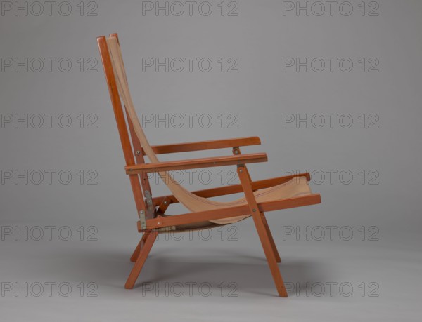 Deckchair, Polish Timber Industry, Czerski and Jakimowicz Lviv; furniture factory; 1929–1939,  furniture factory author; lounge, beach, and garden folding deckchair constructed from two different-sized rectangular frames: the backrest smaller and the seat larger, connected by hinges, with canvas stretched over them. Frame elements except the turned rear leg connector and the doubled front seat stile are angular. The seat frame is supported on its shorter sides by two folding legs connected by a connector, the front extended into armrest supports. The armrests have hinges adjustable in three positions. Salmon-colored canvas fabric with vertical orange stripes framed by narrow blue stripes; canvas attached to the underside of the upper backrest frame and the rear seat frame, sandwiched between the two front seat frames. Originally equipped with a separate footrest. 1938–1939, Lviv; seating furniture, height 84.2 cm, width 58.5 cm, depth 115.5 cm., A wooden folding chair with a slanted ba...
