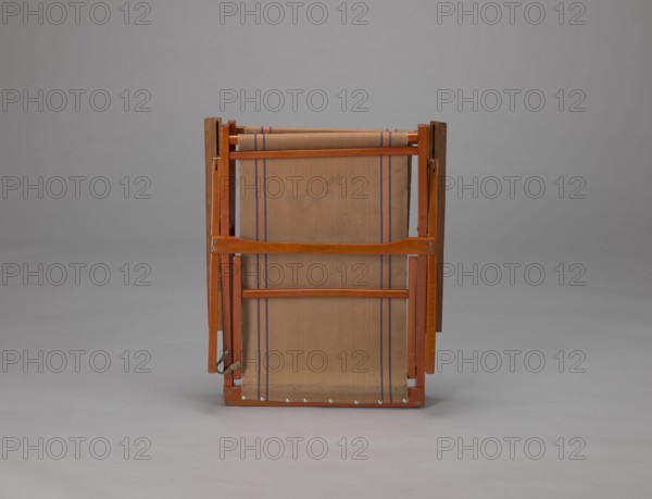 Deckchair, Polish Timber Industry, Czerski and Jakimowicz Lviv; furniture factory; 1929–1939,  furniture factory author. Lounge, beach, and garden folding deckchair constructed from two different-sized rectangular frames: the backrest smaller and the seat larger, connected by hinges, with canvas stretched over them. Frame elements except the turned rear leg connector and the doubled front seat stile are angular. The seat frame is supported on its shorter sides by two folding legs connected by a connector, the front extended into armrest supports. Armrests have hinges adjustable in three positions. Salmon-colored canvas fabric with vertical orange stripes framed by narrow blue stripes; attached to the underside of the upper backrest frame and the rear seat frame, sandwiched between the two front seat frames. Originally equipped with a separate footrest. Date: 1938–1939. Place of origin: Lviv. Type: seating furniture. Dimensions: height 84.2 cm; width 58.5 cm; depth 115.5 cm., A wooden f...