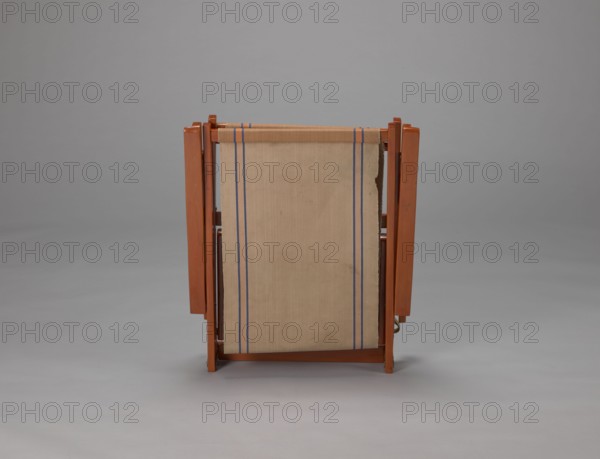 Deckchair, Polish Timber Industry, Czerski and Jakimowicz Lviv; furniture factory; 1929–1939,  furniture factory author; lounge, beach, and garden folding deckchair constructed from two different sized rectangular frames: backrest smaller and seat larger connected by hinges, with canvas stretched over them. Frame elements except the turned rear leg connector and the doubled front seat stile are angular. Seat frame is supported on its shorter sides by two folding legs connected by a connector, the front extended into armrest supports. Armrests have hinges adjustable in three positions. Salmon-colored canvas with vertical orange stripes framed by narrow blue stripes; canvas attached to underside of upper backrest frame and rear seat frame, sandwiched between the two front seat frames. Originally equipped with a separate footrest. 1938–1939, Lviv; seating furniture, height 84.2 cm, width 58.5 cm, depth 115.5 cm., A wooden folding chair seen from the back with a rectangular fabric seat pan...