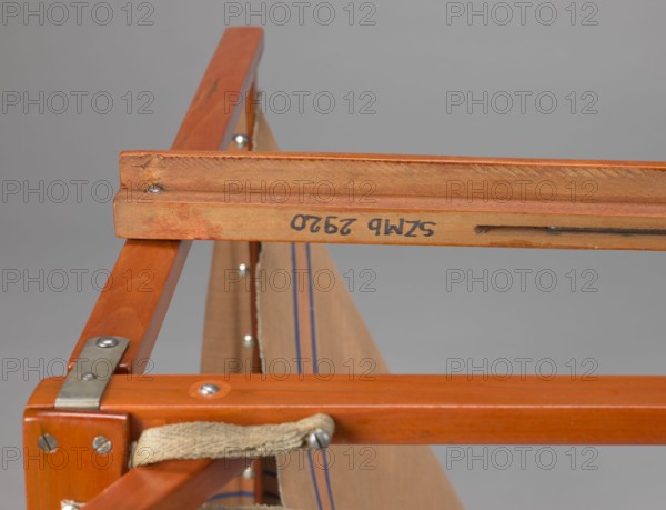 Deckchair, Polish Timber Industry, Czerski and Jakimowicz Lviv; furniture factory; 1929–1939. Folding deckchair constructed from two different sized rectangular frames: the backrest smaller and the seat larger, connected by hinges, with canvas stretched over them. Frame elements except for the turned rear leg connector and the doubled front seat stile are angular. The seat frame is supported on its shorter sides by two folding legs connected by a connector, the front extended into armrest supports. The armrests have hinges adjustable in three positions. Salmon-colored canvas fabric with vertical orange stripes framed by narrow blue stripes; attached to the underside of the upper backrest frame and the rear seat frame, sandwiched between the two front seat frames. Originally equipped with a separate footrest. 1938–1939. Lviv. Piece of seating furniture; height 84.2 cm, width 58.5 cm, depth 115.5 cm., A close-up of a wooden frame showing a group of intersecting wooden slats in warm orang...