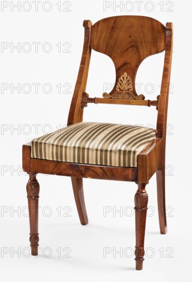 Chair, acanthus ornament, Biedermeier style, palmettes ornament. Front legs straight, turned in the form of a baluster; rear legs sabre-shaped. Trapezoidal seat, slightly bulging at the front. Wide side frames framing the seat cushion. The cushion rests on a pine frame, upholstered in green-striped fabric. Backrest composed of angular, S-shaped side stiles, a lower crossbar, and a rounded central board placed between them, narrowed at the bottom, straight in line with the back. Backrest stiles widened in the lower section, ending at the top with a forward-curved volute. Polished frame enriched with woodcarving—acanthus leaves on the upper part of the front legs, antemion and symmetrical S-shaped beams at the bottom of the backrest boards, scrollwork at the ends of the backrest crossbars. 1830–1840, Warsaw, Poland. Seating furniture, furniture. Height 92.3 cm; width 51 cm; depth 56.5 cm., A wooden chair with a warm brown finish and visible wood grain, featuring a curved backrest with a ...