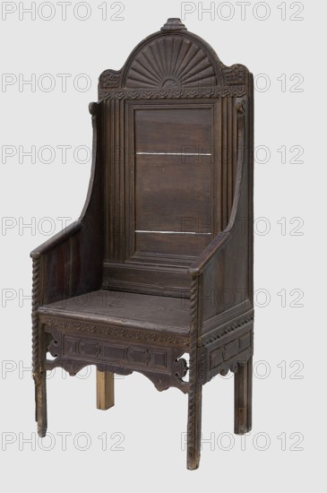 Armchair, geometric ornaments, plant decoration. Armchair with a high rectangular backrest, equally narrow seat and full sides, supported by four angular legs, richly decorated with bas-relief geometric and stylized plant motifs. Framed back, framed on the sides by fluted pilasters, profiled at the bottom, topped with a semicircular top. The top is decorated in the center with a fan with convex wings framed on the sides by wavy corners. The seat and sides are boarded. The sides are arched, with boarded armrests rounded at the corners. Below the frame are decorative strips with geometric fields, wavy at the bottom; the front is suspended, openwork on the sides, and the sides are applied. A strip with a cord motif is applied to the front edge of the legs and sides. Ca. 1635, Netherlands, England, Western Europe. Furniture — seating piece. Height 160.5 cm; width 70.3 cm; depth 51.5 cm., A tall wooden chair with a high back and armrests, carved with decorative patterns including a semi-cir...