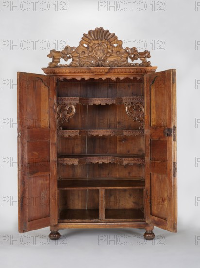 Wardrobe Armoire, rococo ornament, rocaille ornament, plant decoration, rosettes, cuboid, closed with double doors, richly carved, topped with a decorative board with a rococo, asymmetrical cartouche framed with rocaille motifs. Supported by four low legs, the front ones slightly flattened spheres, the rear in block form. Sides of the body and door leaf framed with three flat-carved panels with stylized plant motifs and rosettes against a star-shaped punched background. Frames symmetrically cut on the inside with a wavy profile. Board backs set in a rebate, fastened with dowels and nails; with saw marks. Interior: three narrowed shelves in the middle section with wooden galleries, fourth surface forming top of a compartment containing two drawers at the bottom. Upper shelf rests on openwork consoles with rocaille motifs. Shelves connected to the sides with large-diameter pins approx. 15 mm. Steel fittings; eyelet hinges secondary; push-pull lock not preserved. Late 18th century, France...