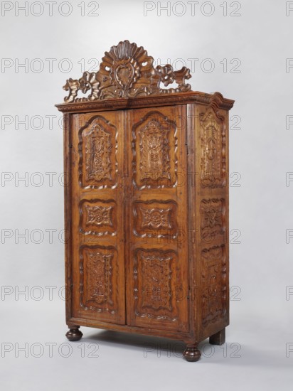 Wardrobe Armoire, rococo ornament, rocaille ornament, plant decoration, rosettes, cuboid closed with double doors, richly carved, topped with a decorative board with an asymmetrical rococo cartouche framed with rocaille motifs. Supported by four low legs, front ones slightly flattened spheres, rear ones block form. Sides of the body and door leaf framed with three flat-carved panels with stylized plant motifs and rosettes on a star-shaped punch background. Frames symmetrically cut on the inside with a wavy profile. Board backs set in a rebate, fastened with dowels and nails; with saw marks. Interior: three narrowed middle shelves with wooden galleries, the fourth being the upper surface of the compartment containing two drawers at the bottom. Upper shelf rests on openwork consoles with rocaille motifs. Shelves connected to the sides with large-diameter pins ~15 mm. Steel fittings; eyelet hinges secondary; push-pull lock not preserved. Late 18th century, France. Furniture; storage furni...
