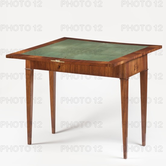 Game table, games, Biedermeier style, rectangular game table with a folding top, supported by four slender, angular, tapering legs, veneered with mahogany. The top rotates on an eccentric tenon, covered on the inside with green cloth enclosed by a mahogany cross frame. Storage compartment inside the case. At the joints of the legs and the case are elongated dice, bordered with petals at the bottom. Date: 1820–1830, Warsaw. Furniture, game furniture. Dimensions: height 78.3 cm, width 89.4 cm, depth 44.4 cm., A wooden table with a green inset surface, showing a rectangular top framed by warm brown wood and supported by four tapered legs in the same brown wood, set against a plain light background.