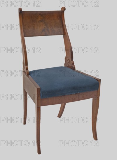 Chair, Biedermeier style, carved rosette and stylized acanthus ornamentation. Chair with an openwork backrest and a trapezoidal padded seat removable cushion. Legs and side frames of the backrest are angular, narrow at the front, wide at the sides. Front legs slightly S-shaped with volutes at junctions to side frames; rear legs arched backward. Side frames are high, encompassing the seat cushion; front and rear rails are low, front rail slightly bulging. Side rails of the backrest are S-shaped, wide at the bottom, carved in relief with rosettes and stylized acanthus leaves, tapering toward the top and topped with forward-curved volutes, glued to the upper edges of the side frames. Backrest board is wide, slightly curved forward at top and bottom, originally enriched with carved decoration above and below. Upholstery fabric not original — navy blue plush. Date: 1820–1840. Place of origin: Vilnius. Classification: seating furniture / furniture. Dimensions: height 89.5 cm; width 46.3 cm; ...