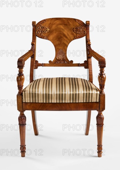 Armchair, Biedermeier style, acanthus ornament, message Office of the Council of Ministers, palmettes ornament. Front legs straight, turned in the form of a baluster; rear legs sabre-shaped. Trapezoidal seat, slightly bulging at the front. Wide side frames framing the seat cushion. Cushion rests on a pine frame, upholstered in green-striped fabric. Backrest composed of angular, S-shaped side stiles, a lower crossbar, and a rounded central board placed between them, narrowed at the bottom, straight in line with the back. Backrest stiles widened in the lower section, ending at the top with a forward-curved volute. Armrests angular, ending in a volute at the front, and with a rolled acanthus leaf at the backrest. Armrest supports turned in the form of a baluster. Polished frame enriched with woodcarving — acanthus leaves on the upper part of the front legs, antemion and symmetrical S-shaped beams at the bottom of the backrest board, scrollwork at the ends of the backrest crossbars. 1830–1...