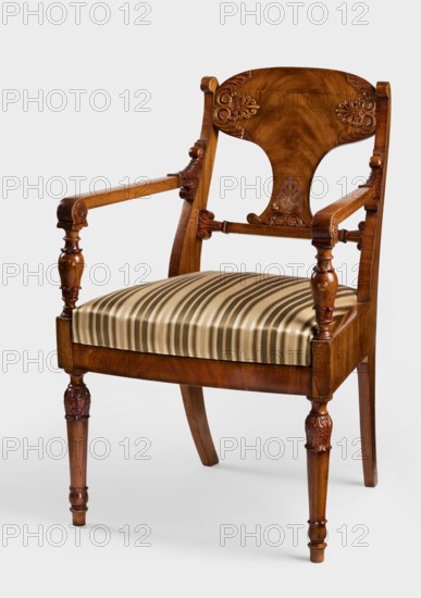 Armchair, Biedermeier style; acanthus and palmettes ornament. Front legs straight, turned in the form of a baluster; rear legs sabre-shaped. Trapezoidal seat, slightly bulging at the front. Wide side frames framing the seat cushion. Cushion rests on a pine frame, upholstered in green-striped fabric. Backrest composed of angular, S-shaped side stiles, a lower crossbar, and a rounded central board placed between them, narrowed at the bottom, straight in line with the back. Backrest stiles widened in the lower section, ending at the top with a forward-curved volute. Armrests angular, ending in a volute at the front, and with a rolled acanthus leaf at the backrest. Armrest supports turned in the form of a baluster. Polished frame enriched with woodcarving — acanthus leaves on the upper part of the front legs, antemion and symmetrical S-shaped beams at the bottom of the backrest board, scrollwork at the ends of the backrest crossbars. Dated 1830–1840, Warsaw, Poland. Piece of furniture, sea...