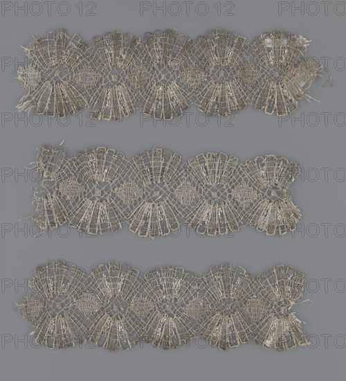 Lace fragment, lace, provenance unknown, metal threads, 18th century, Europe, lace, fabric, width 8.2 cm, length 27.5 cm, A photograph shows three horizontal strips of delicate lace placed against a solid background. The lace strips are off-white or beige with a slightly aged, creamy tone and feature repeated fan-like motifs connected by an open, netted weave. The edges of the lace are scalloped with small loops and some loose threads and frayed ends visible. The background is a uniform medium gray that contrasts with the lighter lace. The overall composition displays the lace pieces arranged with even spacing, showing their intricate woven patterns and the subtle texture of the thread.