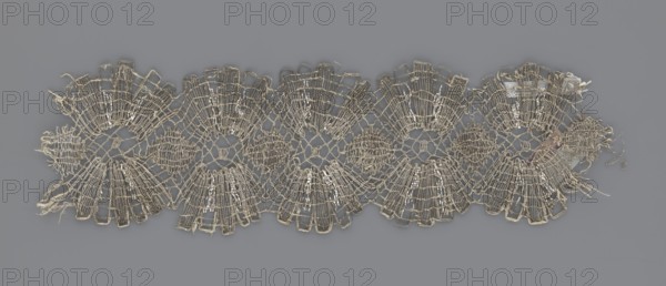 Lace fragment, lace, metal threads, 18th century, Europe, fabric, width 8.2 cm, length 27.5 cm., A length of delicate openwork lace with a repeating scalloped motif, showing a network of fine threads forming fan-shaped and circular patterns; the threads appear frayed in places and some loose ends extend from the edges; the lace is primarily a pale beige or off-white with subtle variations in tone, and there are small shiny silver highlights woven into parts of the design; the background is a uniform mid gray.