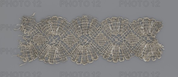 Lace fragment, lace, provenance unknown, metal threads, 18th century, Europe, lace, fabric, width 8.2 cm, length 27.5 cm, A delicate piece of lace with a repeating scalloped pattern laid flat on a gray background, showing a light beige or off-white thread forming intricate openwork with fan-shaped motifs and circular medallions, loose thread ends and frayed edges at the sides, and shiny reflective highlights on some threads against the gray.