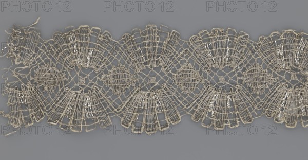 Lace fragment, lace, metal threads, 18th century, Europe, fabric, width 8.2 cm, length 27.5 cm., A strip of delicate openwork lace with a repeating scalloped pattern laid flat on a smooth background; the lace is composed of interconnected mesh and fan-shaped motifs with rounded medallion-like elements between the scallops, and some loose thread ends at one edge. The visible colors include shades of beige and off-white in the lace against a medium gray background.