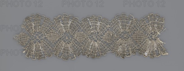 Lace fragment, lace, metal threads, 18th century, Europe, fabric, width 8.2 cm, length 27.5 cm., A decorative horizontal strip of delicate openwork lace in beige and off-white tones lies against a flat gray background; the lace features a repeating scalloped pattern with fan-shaped motifs and circular open centers formed by fine looping threads, several areas showing denser woven sections and a few loose thread ends, and the overall texture appears lightweight and airy with subtle sheen on some thread portions.