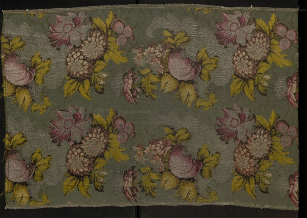 Fragment of patterned silk fabric, 18th century, France. Plant and floral-and-fruit design in a naturalistic style attributed to the influence of French designer Jean Revel; strong chiaroscuro modeling and three-dimensional effect enhanced by abundant silver thread. Background: cannelé 3 coups with an effect described as poil traînant; pattern brocaded with threads tied with a weft weave in light and dark green, yellow, salmon and raspberry pinks, white, silver braided thread, and dark brown/black. Weave: Gros de Tours a effet poil traînant, liseré, broché à liege repris brocade with intercepted broaching threads, type 3. Stiff silk with a grosgrain structure and three-dimensional brocade pattern typical of Lyon silk weaving; pattern type appears from the 1730s and was used for representative court dress Robe à la française. Dimensions: height 97 cm, width 55 cm. Border width: 0.5 x 0.5; width board: 54; report: 44 x 52., A rectangular piece of fabric with a muted green background patt...