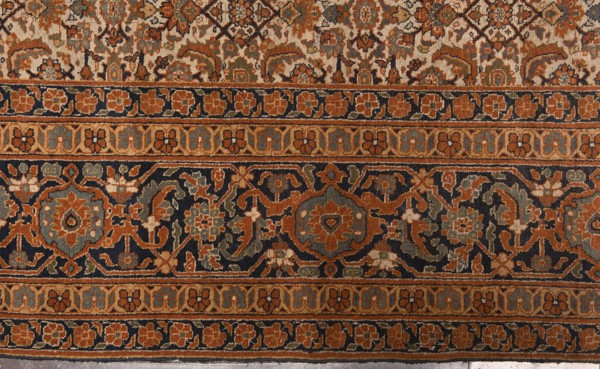 Carpet, 19th century, Iran. Knotted wool carpet with decorative herat-style pattern. Central field on a light cream background with a fine net ornament herat sack composed of lanceolate leaves, rosettes, palmettes, stylized flowers, and rhombuses. Five-band border with floral motifs; widest central band on a navy blue background. Colors: brick red, red, green, blue, navy blue, and white. Function: court and home furnishing. Size: height 520 cm, width 395 cm., The image shows a patterned textile with ornate repeating designs and horizontal bands. The dominant colors visible are rust orange, navy blue, beige, olive green, and muted gray-blue. There is a central dark band filled with floral and geometric motifs in orange, gray-blue, olive, and beige set against a navy background, flanked by narrower bands of small stylized flower shapes in orange and beige on navy and beige backgrounds. Above and below these bands are more intricate areas of interlocking floral and vine patterns in beige,...