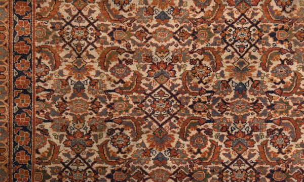 Carpet, Knotted decorative fabric carpet, 19th century, Iran. In the central field on a light cream background: a fine net ornament Herat sack composed of lanceolate leaves, rosettes, palmettes, stylized flowers, and rhombuses. Five-band border with floral motifs; the widest central band on a navy blue background. Colors: brick red, red, green, blue, navy blue, and white. Height 520 cm, width 395 cm., A patterned textile with an ornate repeating design dominated by shades of rust, beige, navy, and muted green, featuring floral and geometric motifs. The surface shows a dense arrangement of stylized flowers, curved leaf-like shapes, and diamond-shaped elements, with darker navy outlines accenting the patterns. Along the left edge there is a vertical border strip with a row of rounded floral shapes on a darker background. The overall texture appears woven or tufted, with subtle variations in color saturation across the design.