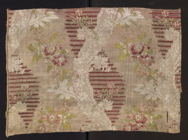 Fabric fragment: patterned silk with floral and lace motifs, mid-18th century, France. Silk fabric fragment, height 54 cm, width 39.5 cm; edge width 0.7 cm; particle width 54., A rectangular piece of woven fabric with a repeating decorative pattern in muted beige and cream background tones, accented by several areas of dusty rose and deep red ribbed shapes, and floral sprays in shades of pink, pale green, and yellow-green; the fabric shows pale lace-like diagonal bands in cream with petal and leaf motifs, scattered clusters of roses and leaves in pink and green, and areas of textured red horizontal ribbing; the edges of the fabric are visible against a dark background and show slight fraying and unevenness, with a narrow gold-yellow trim along one long side.