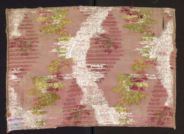 Fabric fragment, silk fabric fragment with floral and lace patterns, mid-18th century, France; silk, patterned; height 54 cm, width 39.5 cm, edge width 0.7 cm., A rectangular piece of woven fabric with a dusty pink background showing a repeating vertical pattern of irregular pale white bands and textured darker pink areas, overlaid with scattered abstract floral shapes in yellow-green and deep red, with areas of frayed or worn threads revealing lighter and darker variations, and a narrow darker border visible along the outer edge; the overall palette includes dusty pink, pale white, yellow-green, deep red, and touches of darker brownish tones.