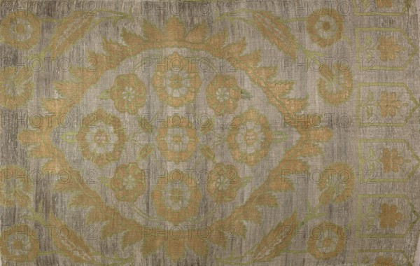 Fabric slab, fragments of a larger textile object, silk fabric, Turkish, 16th century. In the center a large palmette covering the full width, edged with small serrated leaves; inside, symmetrically arranged flat flowers rosettes. In the corners, flower sprigs; on one narrow edge a row of niches each with a central flower. Ornament colors: silver background, gold, and green. Height 103 cm, width 68 cm. Creator, A textured rectangular surface with a worn appearance showing a symmetrical floral and leaf pattern in muted tones; the background is mainly a gray-beige with visible striations, and the decorative motifs appear in shades of gold, light green, and pale beige arranged in a central medallion and repeating border elements, including rounded floral shapes and stylized leaves.