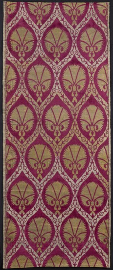 Fabric with a motif of pointed ovals formed from wide ribbons decorated with floral tendrils. Inside the ovals are the calyxes of fan-shaped carnation flowers. Colors of the pattern: red velvet, gold, and beige. Satin and weft weave. Sheared velvet. 16th century, Turkey. Height 153 cm, width 61 cm., A rectangular textile panel with a repeating ornamental motif in shades of deep magenta and gold set against a dark background, the pattern forming teardrop-shaped medallions filled with stylized symmetrical leaf and scroll shapes in gold outlined and surrounded by magenta, interconnected by a lighter decorative lattice of small floral rosettes, the fabric showing variations in texture and slight wear along the edges with a narrow border on one side.