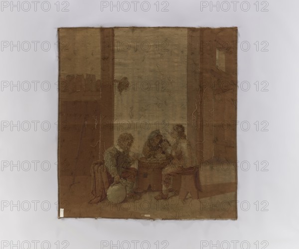 Figural tapestry showing genre scene in an inn. Inside a farm building, perhaps a stable, three men sit at a table made from a sawn-off barrel, drinking and smoking pipes. Above them a hat hangs on a peg under a wooden partition; a wooden walking stick leans against the boards. In the background at left an open door. Fabric without a border. Colors range from beige to light brown, with areas of pink and blue. 18th–19th century, possibly Germany or Flanders. Woven textile, height 175 cm, width 162.5 cm., A rectangular piece of fabric in shades of brown and tan hangs against a pale gray background, showing worn and frayed edges and loose threads across its surface; within the fabric a muted scene rendered in darker and lighter browns and some olive tones depicts a group of seated figures gathered around a central low table or chest, with one figure holding a round object near the floor and another leaning forward toward the center, while architectural elements like vertical panels or col...