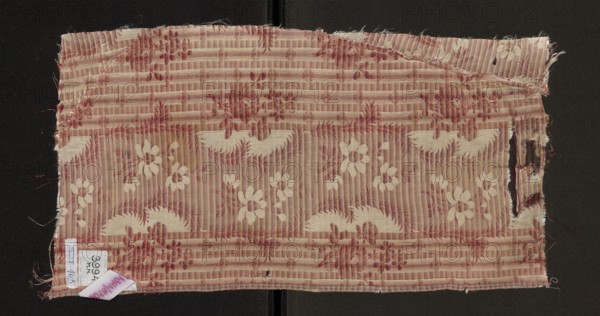Fabric fragment, silk, patterned floral design. Main motif: wide, winding white satin ribbon with projections of flower sprigs with striped petals. Ribbon background shows alternating dark and light salmon-pink horizontal stripes; striped background includes small white flowers, larger flower sprigs, and regularly spaced vertical pink stripes. Construction: background satin with warp-covered fabric; ornament in plain weave. Colors: background in four shades of pink, transverse stripes of twill and pink satin, white satin ribbon along length. Warps in white and pink; wefts bound with a twill weave in three shades of salmon pink and white. Dimensions: fragment 18 x 17.5 cm; overall height 43 cm, width 22 cm. Date: second half of the 18th century. Probable origin: Sweden., A rectangular piece of frayed fabric with a striped woven texture in shades of pink and cream, showing a repeating floral and scalloped motif woven in a lighter cream against a darker pink background; the fabric has une...