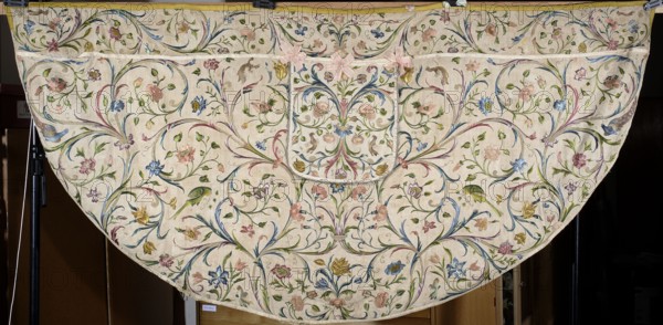 Church cope, Cope made of embroidered silk fabric with linen backing and lining; the original silk backing has crumbled and the embroidery is preserved thanks to an underlying linen backing. Embroidered decoration completely fills the surface with a pattern of leafy tendrils and flowers roses, tulips, carnations. Silhouettes of birds—peacocks, parrots, turkeys, and others—adorn the branches. Edges trimmed with yellow silk braid; hood with preserved bows of pink silk ribbon. 18th century, Silesia. Liturgical vestment. Length 139 cm, width 287 cm., A large semicircular textile with a light cream background covered in an all-over floral and foliate pattern in pastel and muted colors; there are a few shades of pink, blue, green, yellow, and touches of purple and brown in the embroidered flowers, leaves, and curling vines. The fabric shows symmetrical swirling stems and clusters of blossoms and buds, with some small bird shapes worked into the design in green and yellow tones. At the top ed...