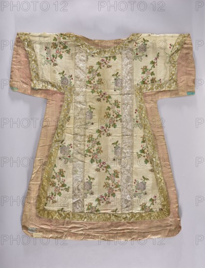 Dalmatic, origin unknown, flowers, leaves, liturgical vestments, plant ornaments, church paraments, sacred art, churches and chapels furnishings, 18th century, France fabric, liturgical vestments, length 101.5 cm, width 92 cm back, A decorative garment laid flat, showing a short-sleeved tunic shape with a wide neckline and a flared lower hem; the main visible fabric is a pale cream or ivory with vertical panels of floral brocade featuring clusters of small flowers in pink, red, green, and muted gold, interspersed with shimmering silver-toned stripes; the cream panels are bordered by a wide metallic gold trim with embroidered floral motifs, and the underlayer and sides of the garment are a soft dusty rose or muted peach silk; the overall surface shows slight wrinkling and the colors present include cream, gold, silver, pink, red, green, dusty rose, and a small area of pale turquoise at one sleeve edge.