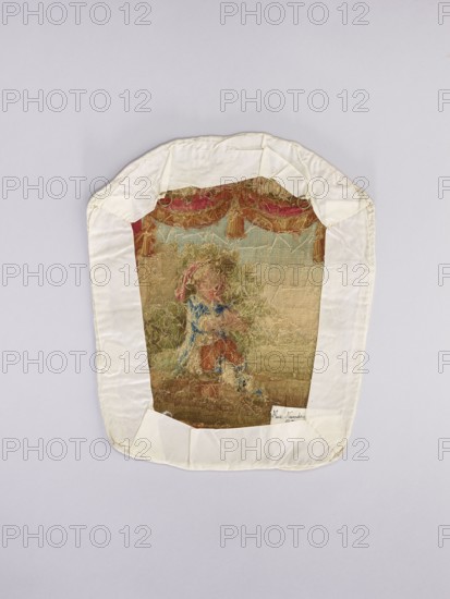 Three tapestry armchair covers, unknown author, varietals, provenance, floral ornaments, genre scenes, interior furnishings, garlands, furniture upholstery, decorative fabrics, tapestries. a boy sitting on a hillock playing a flute; b boy watering flowers; c girl sitting on a hillock. 2nd half of the 18th century, Aubusson; fabrics; height 27.5 cm, width 35 cm., An embroidered textile panel with a white fabric border is shown against a pale gray background; the central embroidered area features muted colors including beige, tan, brown, faded blue, faded red, pink, green, and a few darker browns, depicting a figure in ornate surroundings with draped curtains at the top and textured foliage and ground below, and the white border is folded and stitched at the corners with visible seams.