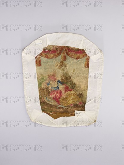 Three tapestry armchair covers, varietals, provenance, motifs: flowers, floral ornaments, genre scenes, interior furnishings, garlands, furniture upholstery, decorative fabrics, tapestries; scenes: a boy sitting on a hillock playing a flute, b boy watering flowers, c girl sitting on a hillock; 2nd half of the 18th century, Aubusson; fabrics; height 27.5 cm, width 35 cm., An irregularly shaped textile piece mounted on a pale background, bordered by a white fabric frame with folded corners; the central embroidered area shows a worn multicolored scene with a dominant palette of muted gold, beige, red, blue, green, and brown, including a group of soft, frayed thread forms suggesting figures and drapery, a decorative scalloped valance in red and gold tones along the upper edge, and areas of loose, tangled fibers and faded stitching across the surface.