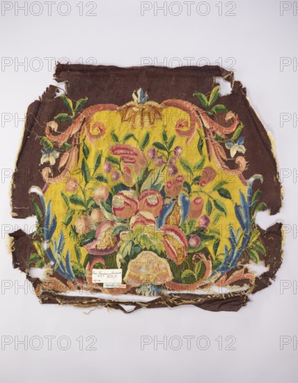 Tapestry upholstery for the seat and backrest of an armchair, unknown author, unknown provenance; design of flowers, floral ornaments, shells, birds; decorative interior furniture upholstery tapestry, function: a seat, b backrest. Surrounded by a frame with motifs of acanthus leaves, shells, and flowers. Colors: brown and yellow background, red, dirty pink, sky blue, green, and yellow-green ornament. Late 18th century, France. Fabric. Height 59 cm, width 57 cm., A worn textile fragment with a central decorative panel featuring a floral arrangement on a bright yellow background, surrounded by a dark brown border; the floral motif includes a group of stylized blossoms and leaves in pink, red, green, blue, cream, and peach tones, with curling ribbon-like elements in soft pink and peach, and accents of darker green foliage and blue elongated leaves, the edges of the fabric are frayed and torn revealing raw threads in beige and yellow, and the overall piece rests on a pale gray background.