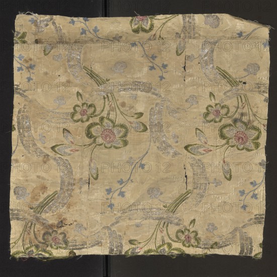 Fabric fragment, fragments of silk patterned fabric, floral pattern, 18th century, France. Weave structure: Gros de Tour background cream warp and weft; pattern - liseré subaperture; brocade wefts: silver lamellar, green, celadon, brown, cherry. Pattern: vertically winding silver ribbon entwined with a sprig of green-silver flowers with brown-cherry centers; vertical arrangement interrupted in places by a horizontally winding silver ribbon creating a network. Colors: cream background; motifs in green, celadon, burgundy, brown. Dimensions: height 50 cm, width 48 cm; edge: 0.7 x 0.8 cm; repeat approx. 50 x 26 cm., A square piece of fabric laid flat showing a floral woven pattern on a pale beige background with a slightly shiny texture; there are a few large stylized flowers with rounded petals in shades of green and pink, accompanied by elongated leaves in green with touches of pink, and flowing curved bands filled with silvery threads; small sprigs with small leaves in light blue are sc...