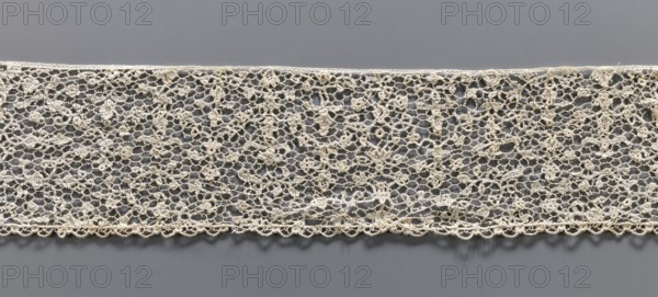 Lace fragment, Lace with a fine floral pattern. de brides background with picots. Lower edge with fine serrations, upper edge straight. 17th/18th century, Venice. Lace, fabric; width 9.5 cm, length 134 cm., A horizontal strip of delicate openwork lace laid flat against a smooth background, showing an intricate network of interconnected loops and floral-like motifs; the lace appears off-white or cream with slight variations in tone, and the background is a uniform medium gray; the lace edges include a scalloped border along the bottom and a straighter edge along the top, and the texture of the thread and tiny knots are visible across the pattern.