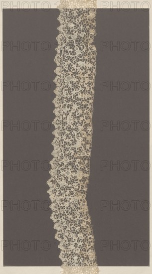 Lace fragment, needle-stitched lace, Krzeszowice Lesser Poland Voivodeship. Sewn in two parts. With motifs of small floral sprigs, flower-rosettes, leaves, and rhombuses filled with openwork. Motifs connected by spans with picots. Lower edge serrated in a wavy pattern with a motif of small palmettes; upper edge plain, unfinished. 17th–18th century, Venice. Lace, length 78 cm, width 6 cm., A narrow vertical strip of intricately patterned lace in off-white and cream tones runs down the center of the image against a dark gray rectangular background, with the lace showing a delicate openwork of loops, floral-like motifs, and scalloped edges; the surrounding outer border is a light beige that frames the darker rectangle.