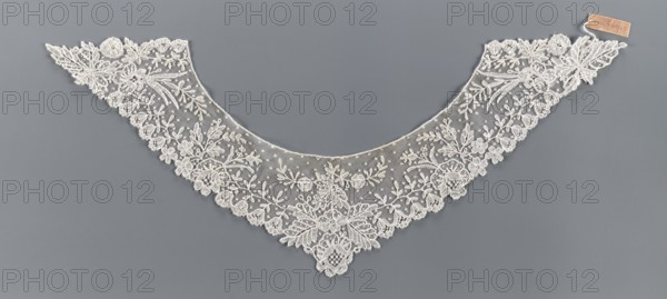 Collar; bobbin lace; 19th century, Europe. Floral ornament includes various types of flower rosettes: small 5-leaf rosettes, larger feathery ones at the corners, bell-shaped calyxes with a stripe on the edges, small lanceolate and larger divided leaves. Women's clothing accessory; lace collar. Dimensions: width 11 cm, length 34.5 cm., A delicate triangular lace collar laid flat against a solid background, featuring an open netted base embroidered with an intricate floral and leaf pattern; the lace shows scalloped edges with clusters of embroidered flowers, leafy sprigs, and ornate botanical motifs that become denser toward the central point, and a small rectangular attachment at one end. The visible colors are off-white for the lace, a muted gray for the background, and a light tan on the small attachment.