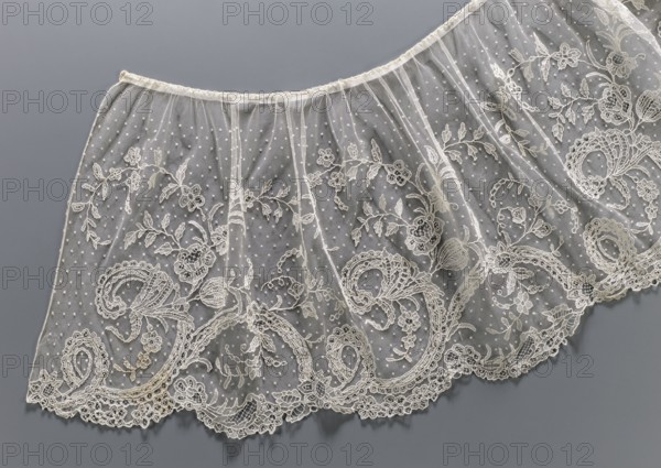Collar, Lace collar so-called berta with a pattern of flowers, leaves and small dots in the background; floral and plant ornaments; clothing accessory for women's clothing; lace; width 33 cm; 1840–1860; Brussels ., A delicate sheer fabric panel with intricate embroidery spread against a smooth background, showing a scalloped edge with ornate lace motifs and swirling floral patterns; the netted ground has a dotted texture and vertical gathers creating soft folds, with embroidered leaves, flowers, and curved paisley-like designs woven into the border and extending upward; visible colors include cream and off-white threadwork on a gray background, with subtle shadows and highlights adding depth.