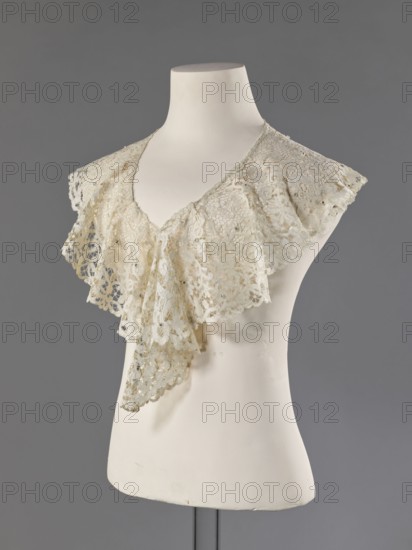 Collar, late 19th century, France. Floral ornaments; fashion; women's fashion; lace collar with mesh connections of large meshes; collar sewn with small beads from a polished edge. Materials: lace; clothing accessory. Dimensions: width 15 cm, length 230 cm., A white mannequin torso displays a delicate lace collar draped around the neck, the lace appearing cream to off-white with intricate openwork patterns and scalloped edges; the collar forms layered ruffles that hang down the front, showing floral and geometric lace motifs and small reflective embellishments scattered across the fabric; the mannequin is matte white and set against a neutral gray background.