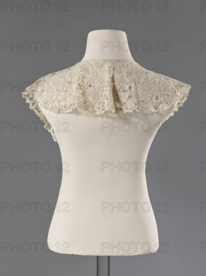 Collar; maker, floral ornaments; fashion; women's fashion; lace; lace collars; mesh connections with large meshes; collar sewn with small beads from a polished edge; late 19th century; France; clothing accessory; lace; width 15 cm; length 230 cm., A mannequin torso in an off-white color is shown from the back against a gray background, wearing a delicate lace capelet in a pale cream to beige tone with an openwork floral pattern and scalloped edges; the lace has a slightly aged appearance with small shiny embellishments scattered across it, and the mannequin surface shows subtle texture and minor marks.