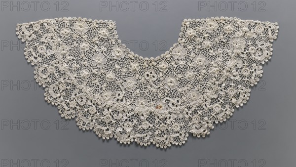 Collar, origin unknown, women's clothing accessory. Needle lace collar with floral tendril pattern featuring large partially raised flowers on a mesh background. Diamond mesh finished with single or triple picots imitating leaves; serrated edges. Collar sewn from two pieces, extended at the bottom. 19th century, Europe. Width 33 cm, length 97 cm., A wide, semicircular piece of delicate lacework with an open, netlike background and an overall light cream color is displayed against a smooth medium-gray backdrop; the lace features a repeating arrangement of ornate floral and circular motifs, raised rosette details, looping ribbonlike shapes, and scalloped edges with small rounded picot trims, creating a layered, textured surface with areas of dense stitching alternating with more open mesh, and the composition forms a curved neckline-like shape with symmetrical extensions on either side.