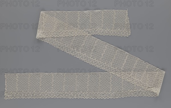Lace fragment, a strip with a serrated edge on one side and an edge-type ornament on the serrated side, above which are narrow strips of stylized plant ornament with an onion-shaped flower motif and between them small round dots in a regular pattern against a mesh background; lace, fabric; 1st half of the 19th century, Europe; width 12.5 cm, length 210 cm., A long strip of delicate lace in an off-white or ivory color lies arranged in a zigzag across a smooth gray background; the lace has a sheer mesh field dotted with small raised points and vertical wavy embroidered lines, bordered along one edge by a scalloped floral trim with looping motifs, and the fabric shows fine netting texture, slight folds, and soft translucent areas where layers overlap.