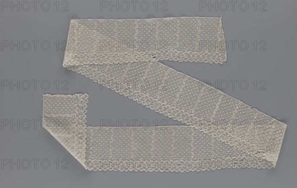 Lace fragment, a strip with a serrated edge on one side and an edge-type ornament on the serrated side; above this are narrow strips of stylized plant ornament with an onion-shaped flower motif and small round dots in regular progression against a mesh background. Lace, fabric; 1st half of the 19th century, Europe. Width 12.5 cm, length 210 cm., A length of delicate lace ribbon is arranged in a zigzag across a smooth background; the lace is pale ivory with a pattern of small dotted mesh and vertical decorative lines, scalloped edges with floral-like loops, and areas where the fabric overlaps creating subtle variations in translucency; the background is a uniform medium gray.