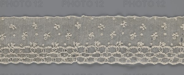 Lace fragment, lace, Edge ornament on one side - a kind of net with numerous loops, small round and slightly larger oval ones, into which small twigs are woven. Above the edge ornament, against the netting background, in regular projections alternate: a twig and a round point. 18th–19th century, France; materials: lace, fabric; width 8.5 cm, length 408 cm., A length of delicate lace with a hexagonal net background in an off-white or cream color laid across a flat gray surface; the lace features a pattern of small floral motifs made from looped thread scattered across the net, a scalloped lower edge with a more densely worked band of looping and oval designs, and a gently scalloped top edge with tiny looped accents, showing texture and fine threadwork in cream against gray.