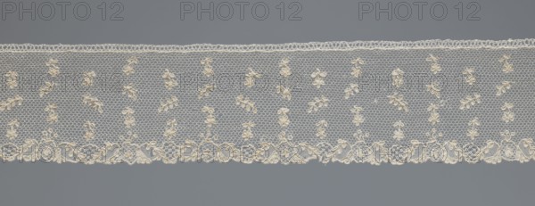 Fragment of lace;, One-sided strip of edge ornament made of plant forms: motif of a pinnately leafed twig. Above the edge ornament, against a mesh background in projections, an alternating twig with a single flower and a pinnately leafed twig. 18th century, France. Lace; width 6 cm, length 63 cm., A horizontal strip of delicate lace displayed against a uniform background, showing a repeating hexagonal net pattern with small floral motifs embroidered throughout and a more elaborate scalloped border along one edge; the lace appears in shades of off-white and cream while the background is a muted gray.