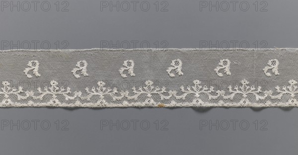 Lace fragment, Plant ornaments, Louis XVI style. At the lower edge there are two trails of fine tendrils, and between them a net with issgrond, mesh. Above, a net with drochelle mesh, on it projections of leafy branches. Contours of motifs reinforced with thread. Late 18th century, Mechelen. Malines lace. Lace, width 7.5 cm, length 146 cm., A horizontal strip of delicate lace in off-white stretched across a smooth gray background, featuring a netted upper field with a row of small ornamental motifs and a lower scalloped border with an ornate floral-like embroidered pattern, the lace showing fine openwork, looping threads, and a small area with a darker ochre discoloration near the bottom edge.