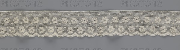 Lace fragment, tied in the form of a belt with one-sided arched serrations. Regular ornament: rosettes and points arranged in rows. Mid-19th century, Flanders, lace, width 7 cm, length 223.5 cm., A horizontal strip of delicate lace is shown against a flat gray background, with the lace in an off-white or cream color featuring a repeating pattern of floral motifs connected by a net-like mesh and small circular accents, the lower edge forming a scalloped border with tiny looped fringes, and the overall texture appearing fine and intricate.