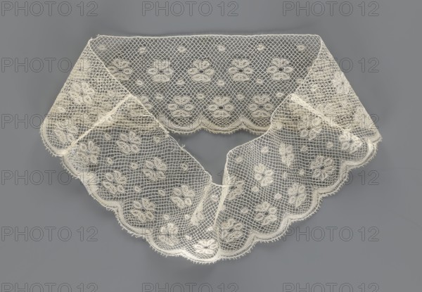 Fragment of lace, section of a belt sewn into a closed circle with one-sided arched serrations. Regular ornament: rosettes and points arranged in rows. Mid-19th century, Flanders . Lace, width 7 cm, length 50 cm., A delicate lace collar displayed against a gray background, made of off-white or cream netted fabric with a repeating floral motif and small circular accents; the lace has a scalloped outer edge and a geometric mesh pattern between the floral elements, with gently folded sections creating soft curves and light shadows.