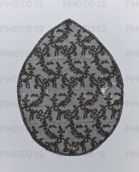Lace, lace, plant ornaments, in the shape of an oval pointed on one side. A narrow strip of geometric ornamentation on the outer edge. The form field is filled with leafy and floral tendrils forming a kind of net fond de Tulle. 19th century, France, fabrics, height 46 cm, width 35 cm, An oval lace fabric piece with a scalloped edge displayed against a pale gray background, featuring a repeating floral and vine pattern in dark brown thread on a sheer gray mesh; the lace shows a few areas of wear with small irregular gaps and a tiny metallic brownish-gold speck near the lower edge.
